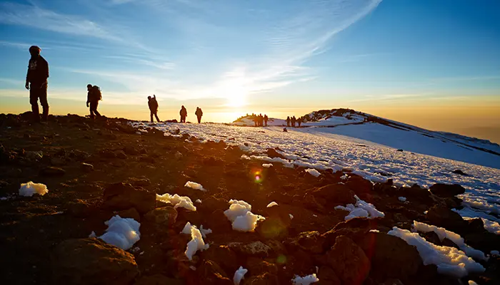 Silhouettes of climbers walking on Kilimanjaro at sunrise, representing extraordinary achievement.